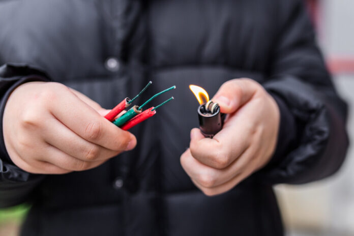 Boy lighting up several firecrackers in his hand using lighter. Kid getting ready for celebration with fireworks or pyrotechnic products . Boy holding a burning petard in his hand. Close up shot