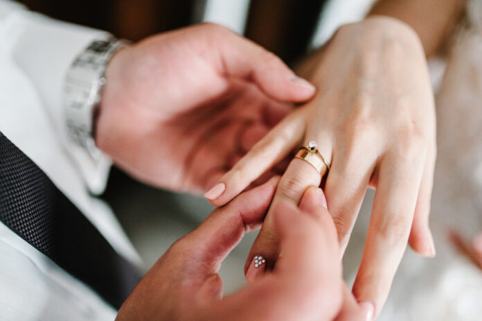 The hands of the groom wears a wedding engagement ring on the fi