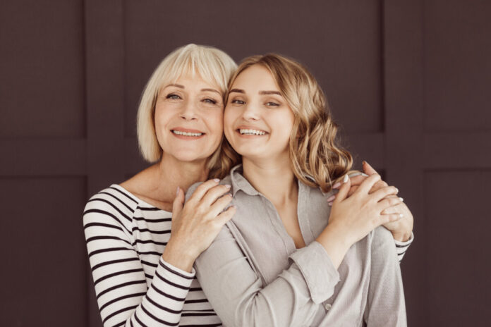 Senior woman and young daughter hugging against brown wall
