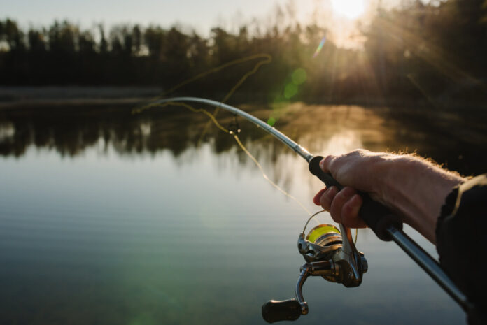 Fisherman with rod, spinning reel on the river bank. Sunrise. Fi