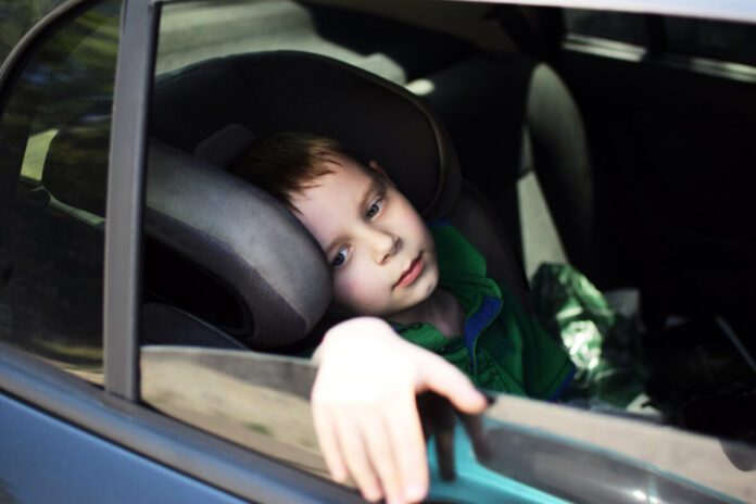 The boy is hot in the car. The child is tired during the trip.