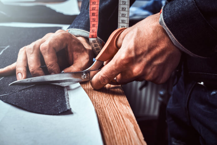 Fashion designer is cutting off fabric with scissors.