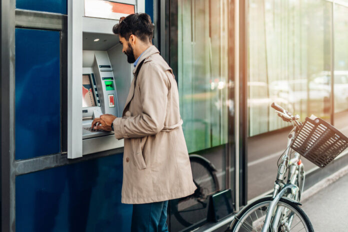 Young bearded man using atm machine to withdraw money.