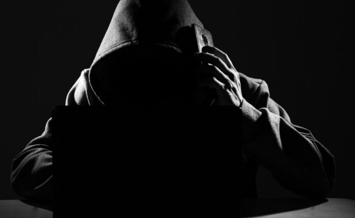Hacker Using Smartphone. Men in black clothes with hidden face.