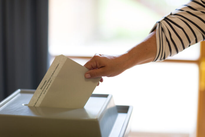 Stimmzettel wird in Wahlurne geworfen